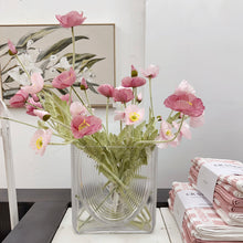 Load image into Gallery viewer, Clear glass vase with assorted coloured poppies on a white surface, with folded pink and white fabric in the background.
