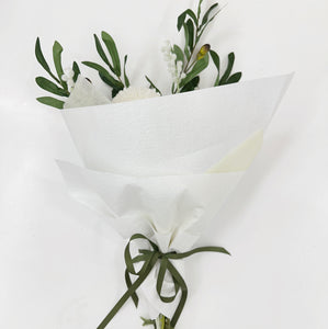 Bouquet of white flowers with green leaves wrapped in white paper on a light gray background