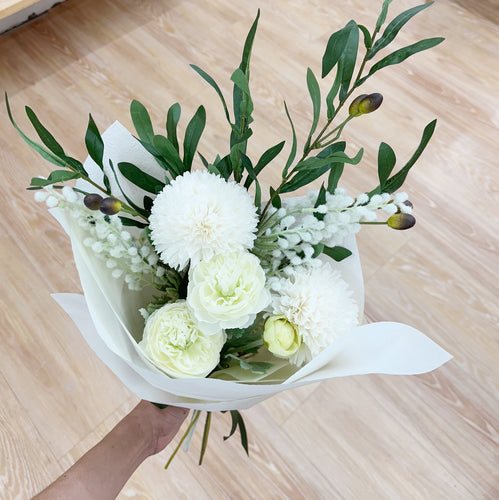 Bouquet of white flowers with green leaves on a wooden surface